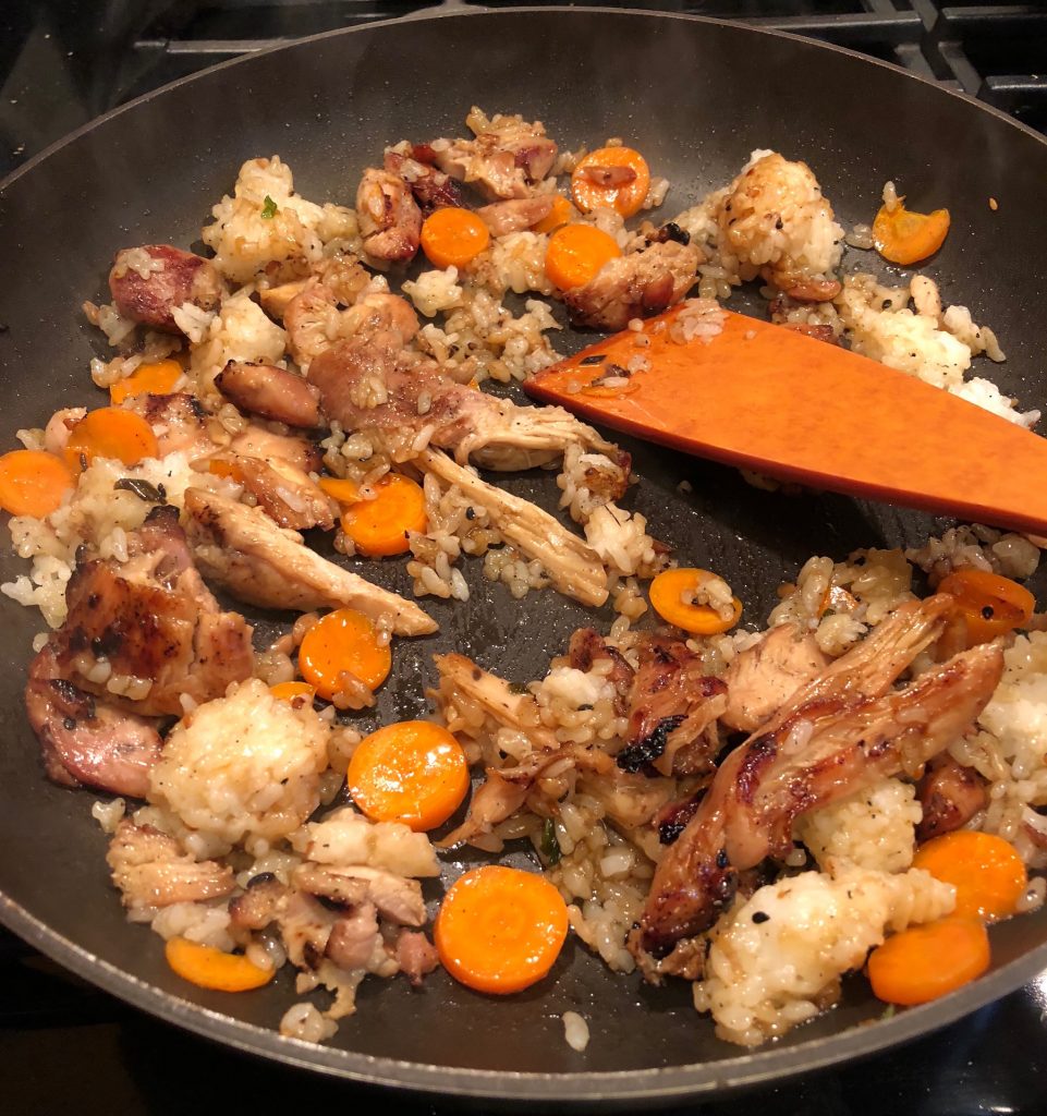 Leftover teryaki chicken, rice, and carrots being stirred together in a black skillet.