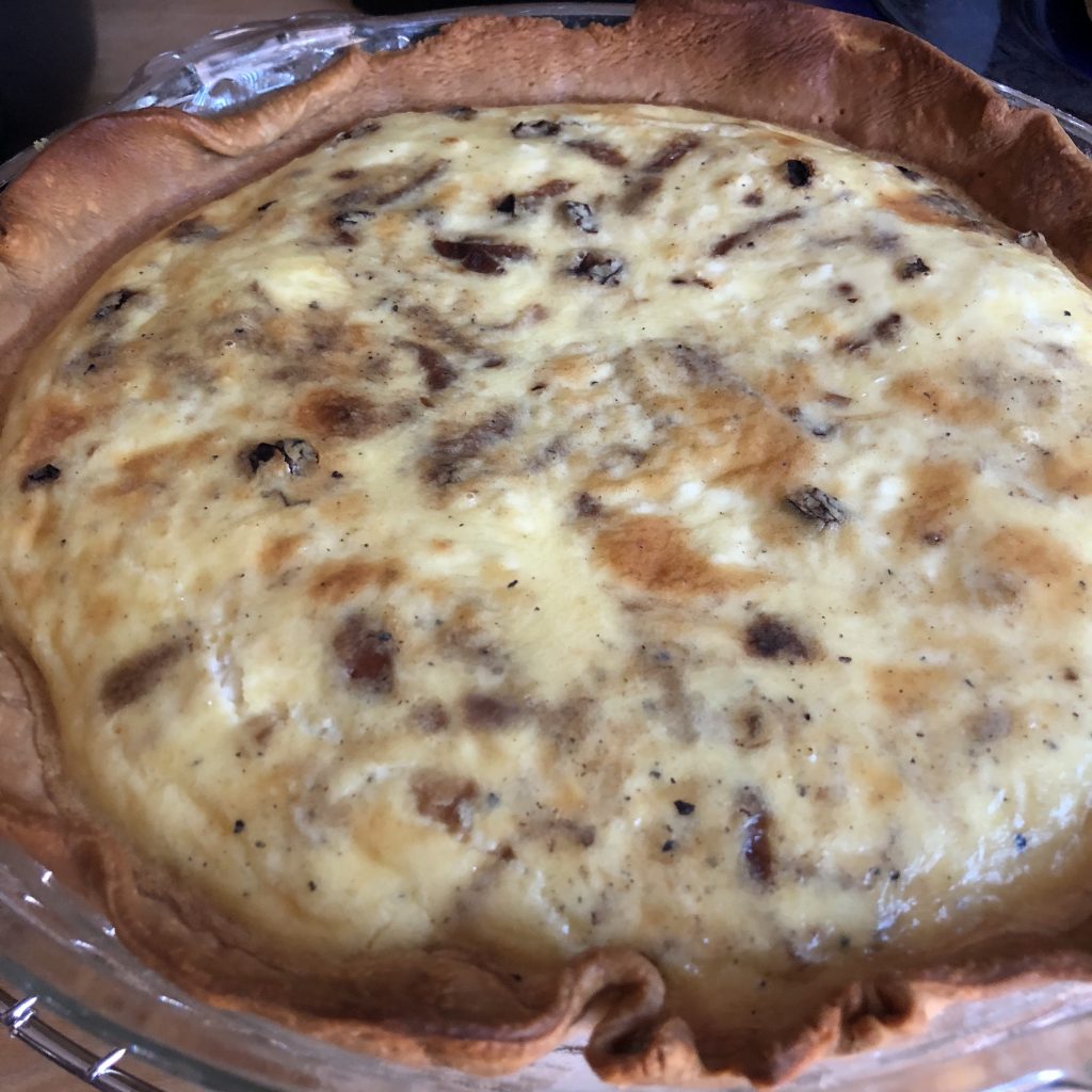 A quiche just out of the oven, studded with brown spots from caramelized onions and browning from the oven.